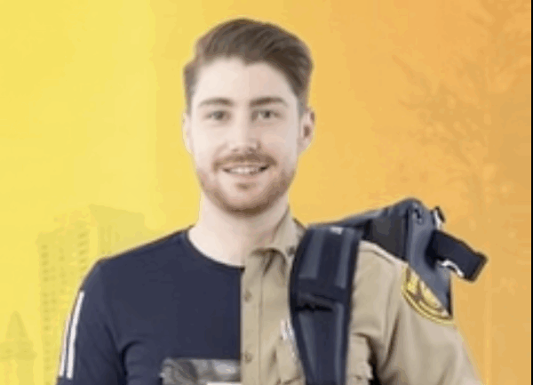 A man stands against an orange background, wearing half a police uniform and half casual clothing, with a police radio on his shoulder.